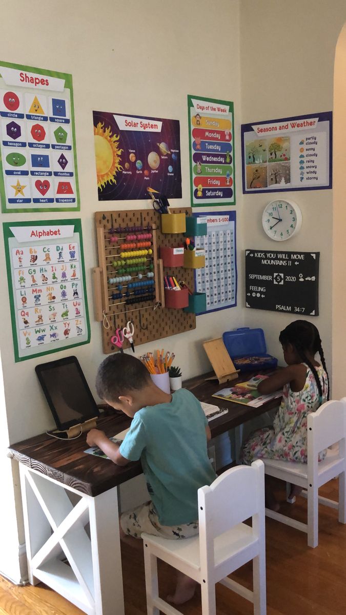 two children are sitting at a desk in front of a wall with posters on it