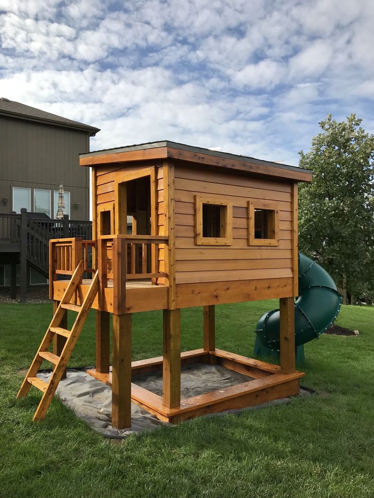 a wooden play house with a slide in the back yard