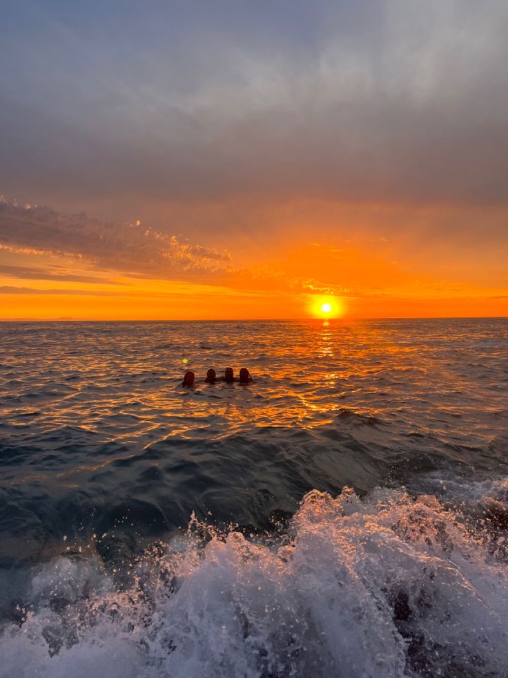 the sun is setting over the ocean as people swim in the water on their rafts