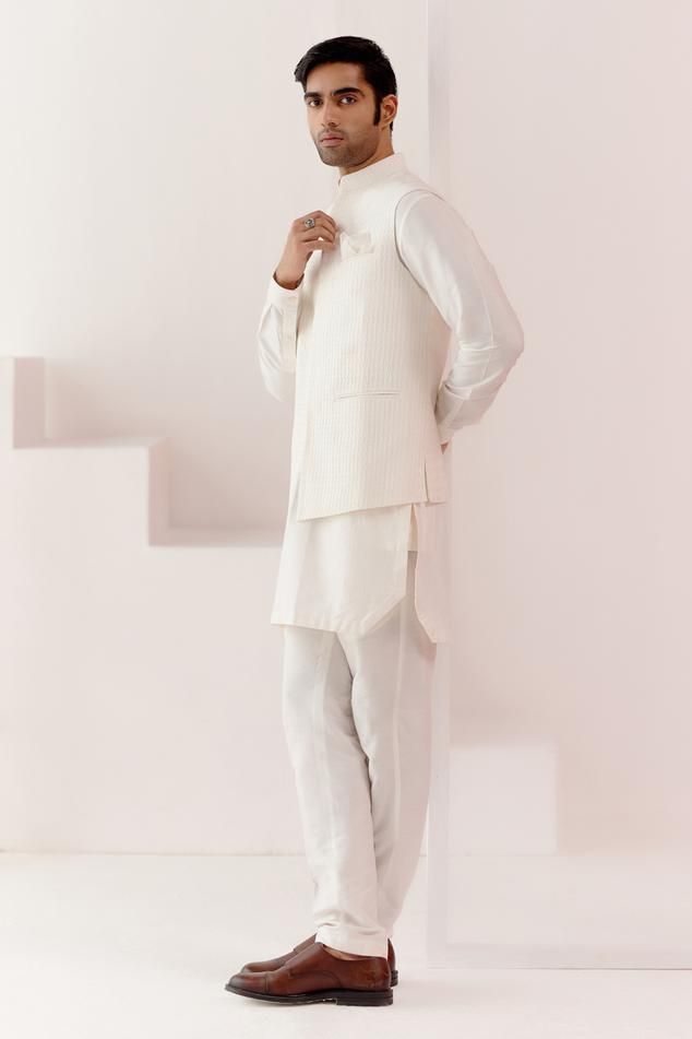 Ivory bundi with all over pintuck pattern. Paired with an inner kurta in stripe pattern and pant. Comes along with a pocket square.
Components: 4
Pattern: Pintuck, Stripe
Neckline: Stand Collar
Sleeve Type: Full Sleeves
Fabric: Cotton Silk Blend
Color: Ivory
Other Details: 
Model height: 5ft 11inches, wearing size M
Occasion: Sangeet - Aza Fashions Elegant Cotton Nehru Jacket With Chikankari Embroidery, Off White Naqshi Bandhgala, Elegant Cotton Nehru Jacket For Eid, White Cotton Nehru Jacket, Classic White Sets For Eid, White Classic Kurta For Formal Occasions, White Cotton Nehru Jacket For Festive Occasions, Elegant White Cotton Nehru Jacket, Festive White Cotton Nehru Jacket