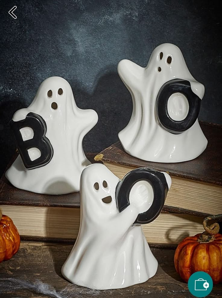 three white ceramic ghost bookends sitting on top of a wooden table next to pumpkins