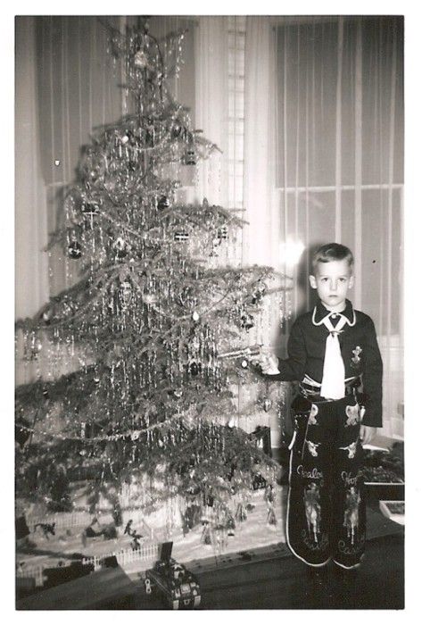 black and white photograph of a young boy standing in front of a decorated christmas tree