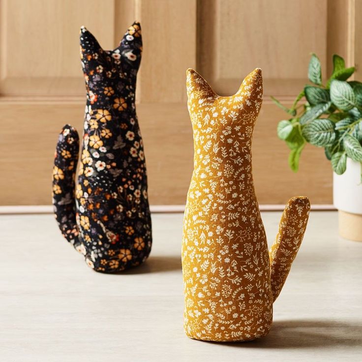 three cat figurines sitting on top of a table next to a potted plant