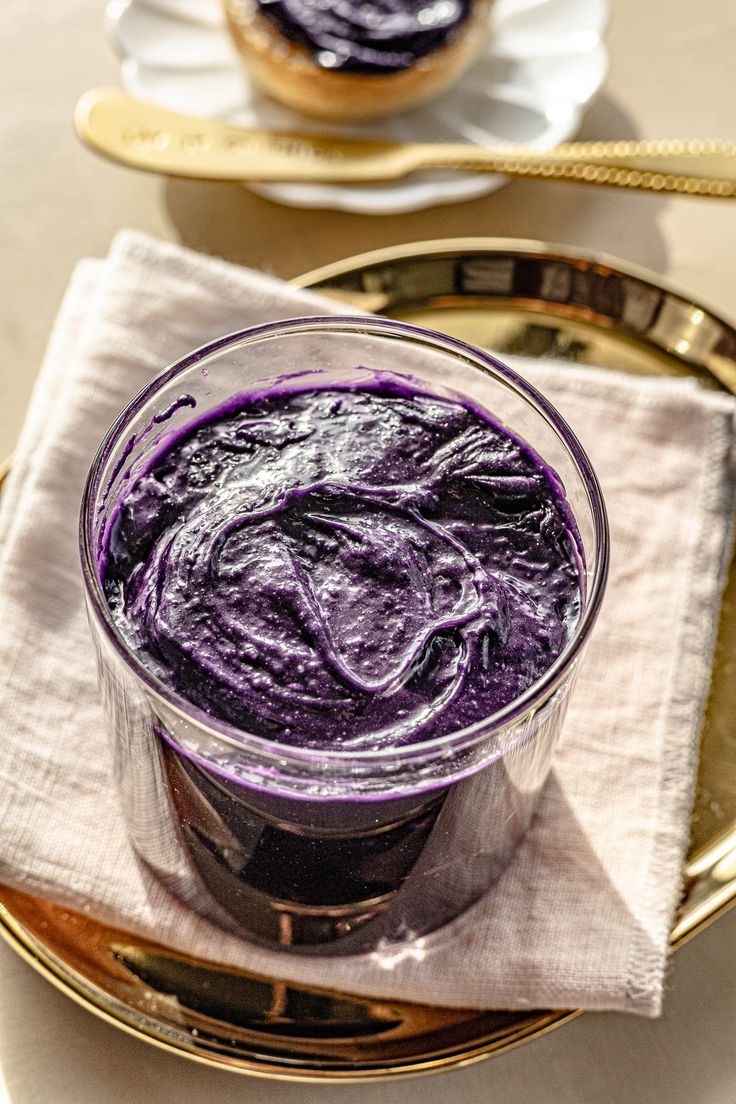 a purple dessert in a glass on top of a gold plate next to a white napkin