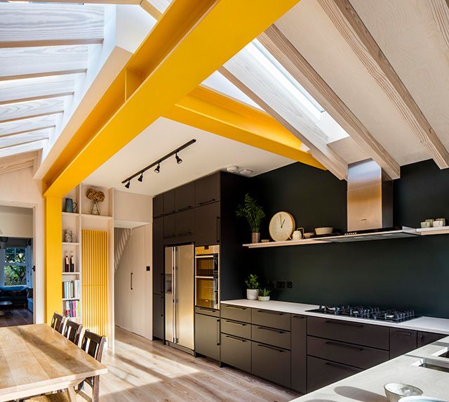 an open kitchen and dining room area with yellow painted beams on the ceiling, along with wooden flooring