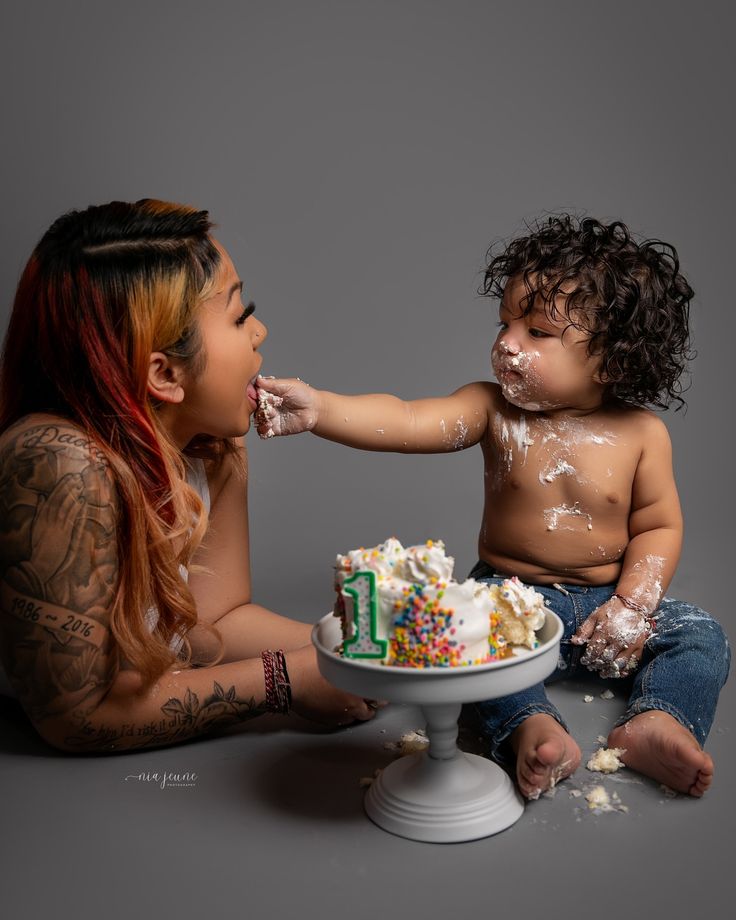 a woman feeding a cake to a baby with sprinkles on his face