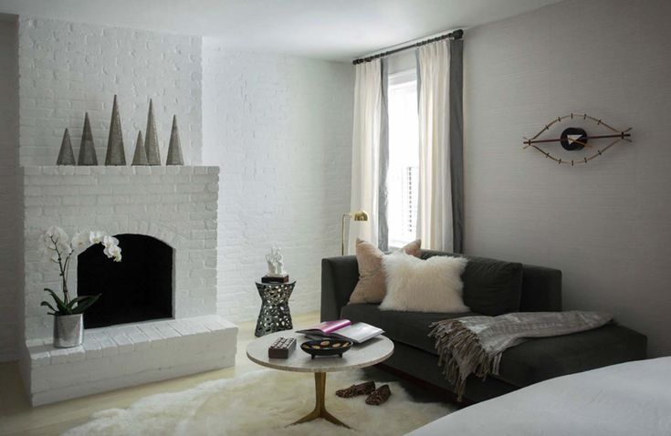 a living room filled with furniture and a fire place in front of a white brick wall