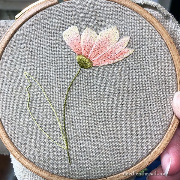 a person holding up a small embroidery project with a flower on it's side