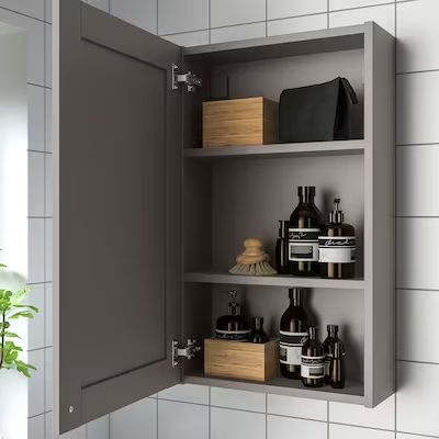 an open medicine cabinet next to a potted plant in a white tiled bathroom area