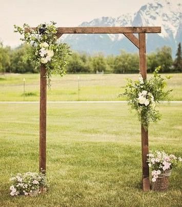 an outdoor ceremony setup with flowers and greenery on the grass in front of mountains