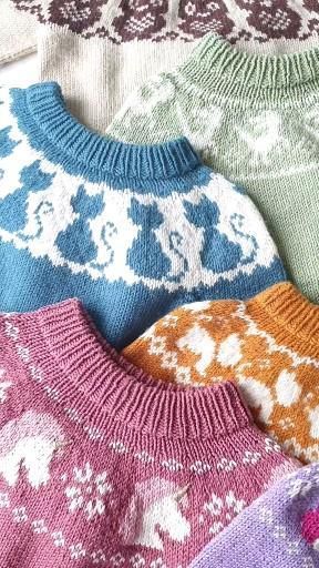 four knitted sweaters are lined up on a table with the colors of them