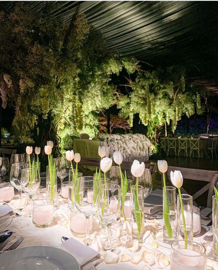 a long table is set up with white flowers and place settings for an outdoor dinner