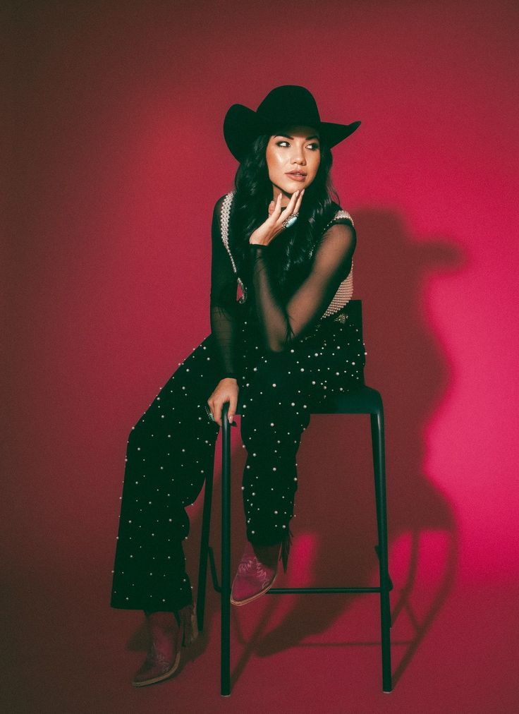 a woman sitting on top of a chair wearing a black hat and polka dot pants