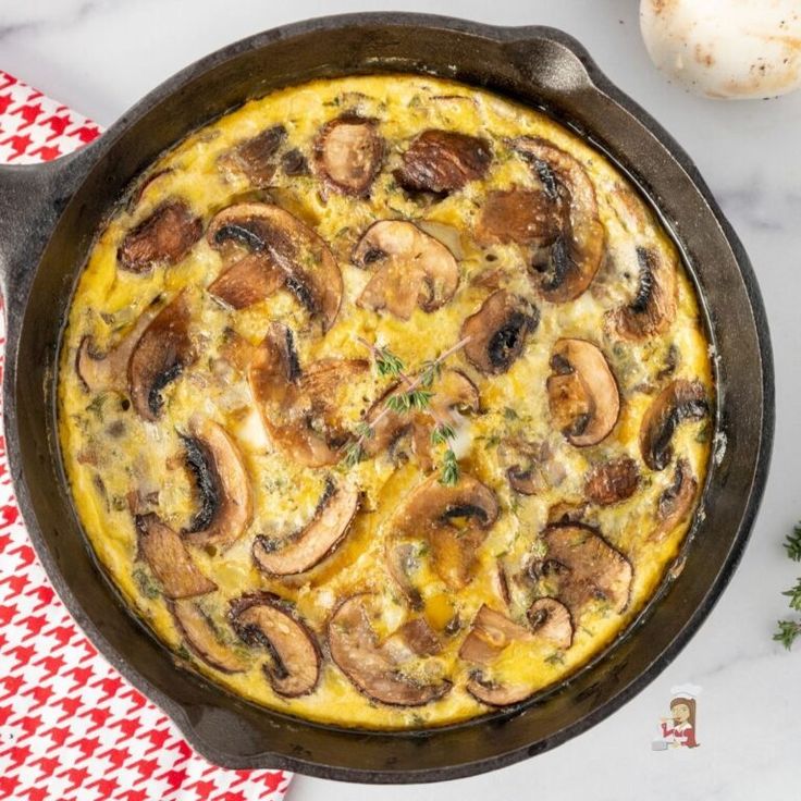 an omelet with mushrooms in a cast iron skillet on a red and white checkered napkin