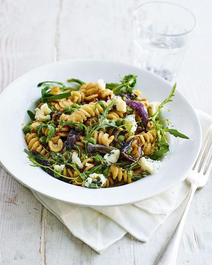 a white bowl filled with pasta and vegetables on top of a table next to a glass of water