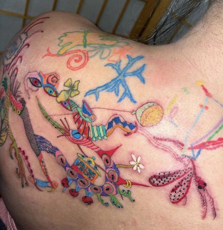 the back of a woman's shoulder with colorful tattoos on her arm and chest