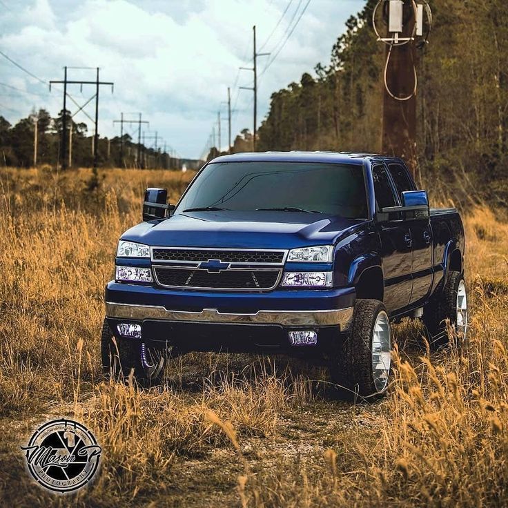 a blue truck parked on top of a dry grass field next to a telephone pole