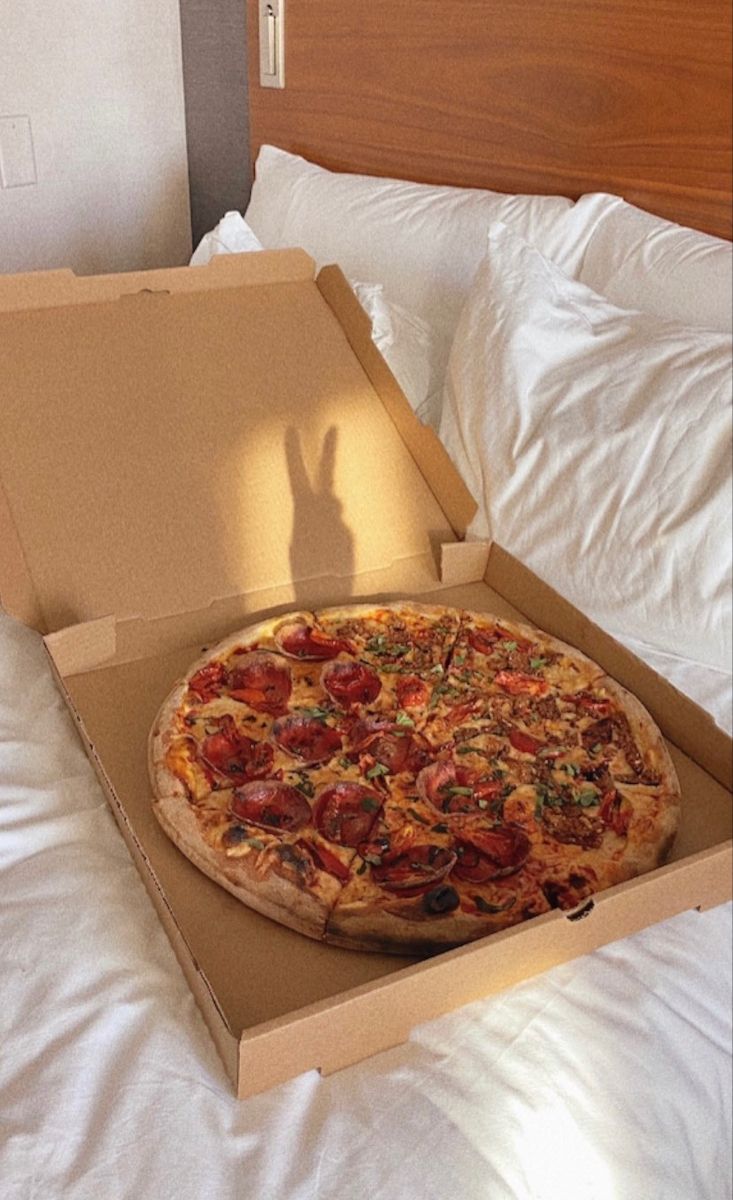 a pizza in a box sitting on top of a bed