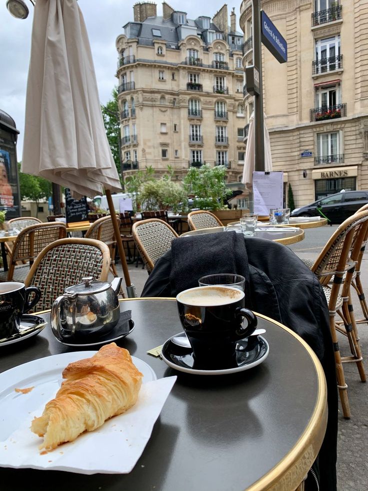 there is a croissant and coffee on the table in front of some buildings