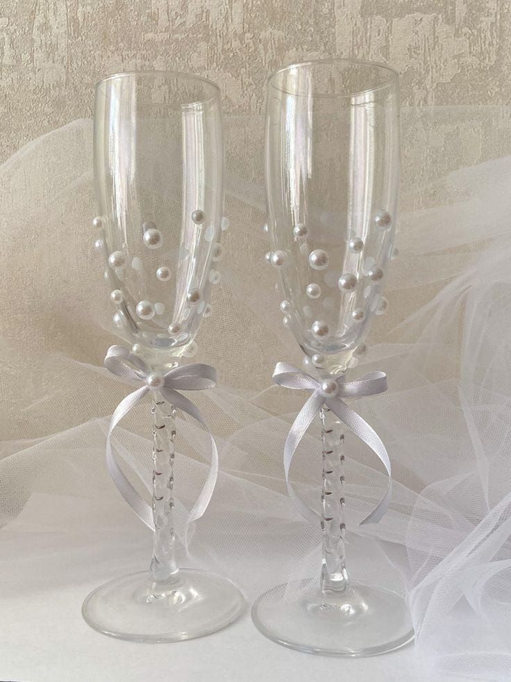 two wine glasses with bows and pearls on the rims are sitting next to each other