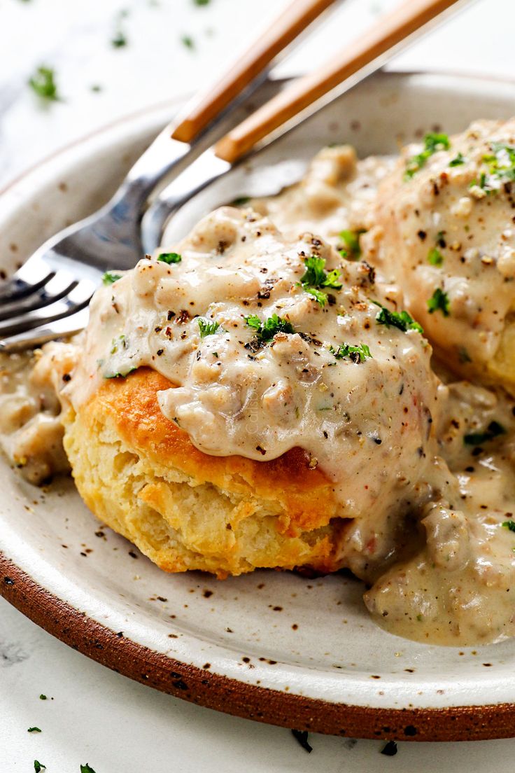 two biscuits covered in gravy on a plate with a fork next to it