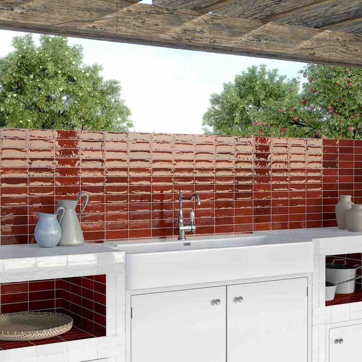 an outdoor kitchen with red tiles on the wall and white cupboards, sink and dishwasher