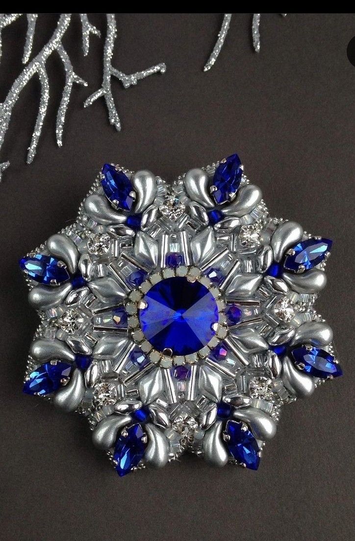 an elaborate brooch with blue and silver accents on a black surface, surrounded by snowflakes