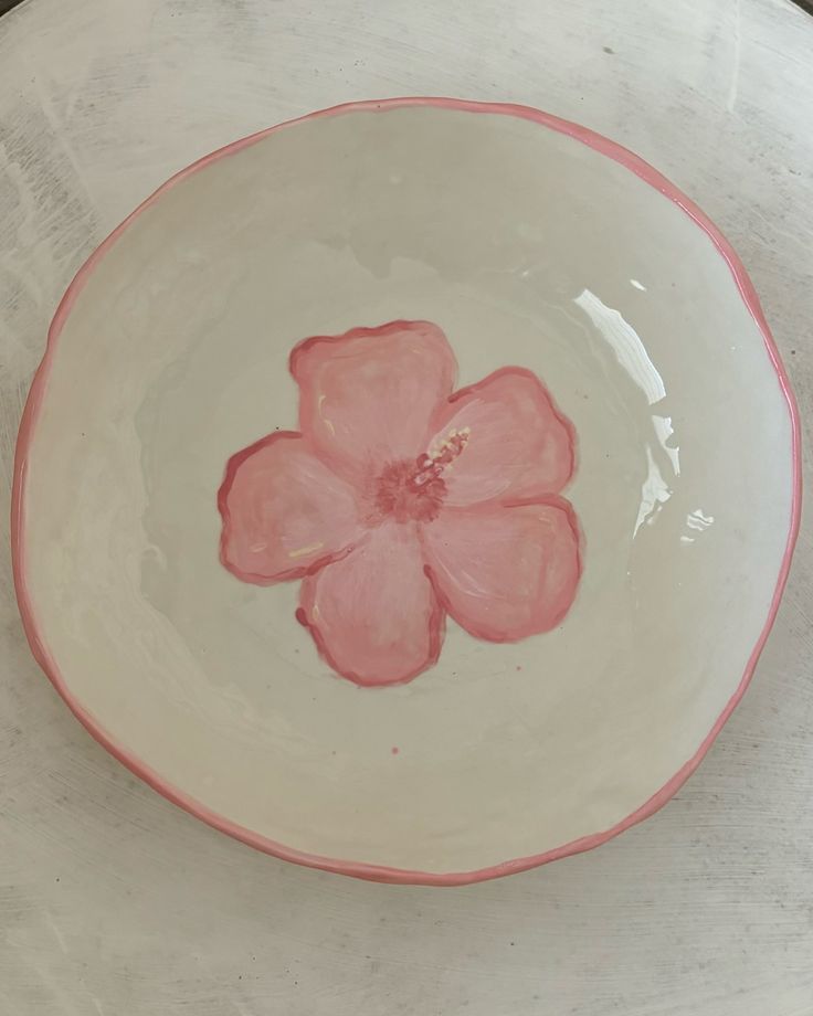 a white and pink bowl with a flower painted on the side, sitting on a table