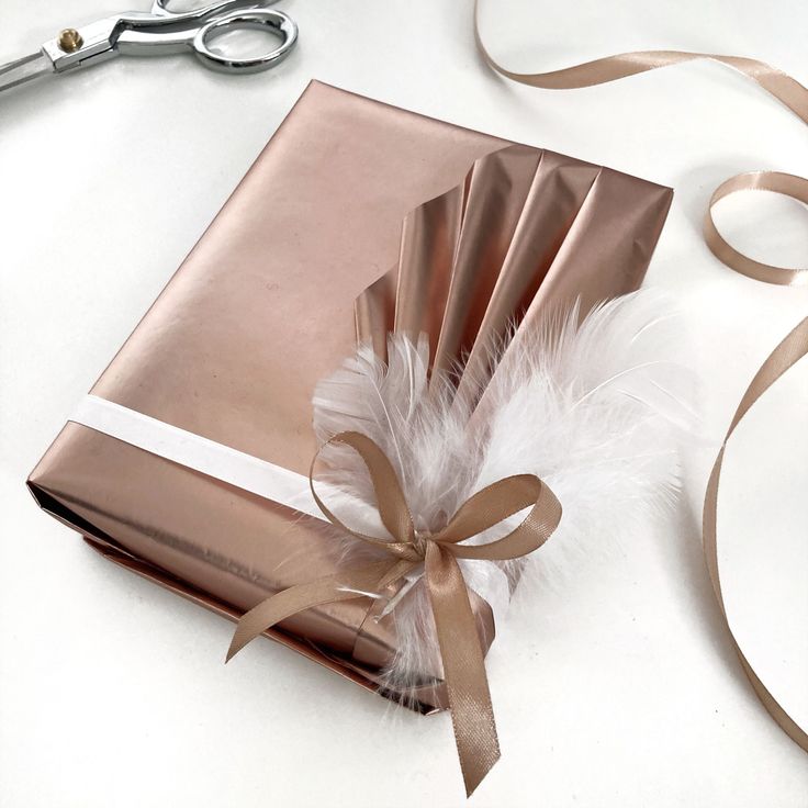 a gift wrapped in copper paper with a ribbon tied around it and a pair of scissors next to it