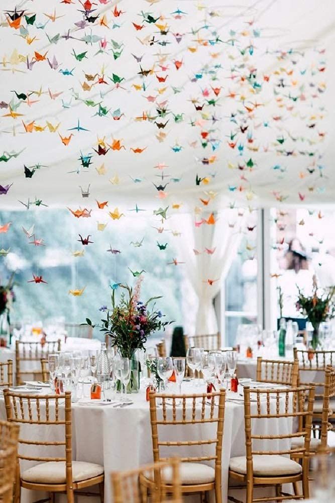 a room filled with lots of tables covered in white linens and paper cranes hanging from the ceiling