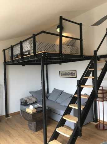 a loft bed with stairs leading up to the top floor and couch below it in a living room