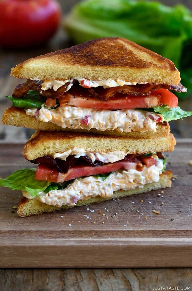 two sandwiches stacked on top of each other with lettuce and tomatoes in the background