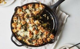 a skillet filled with food on top of a white table next to plates and utensils