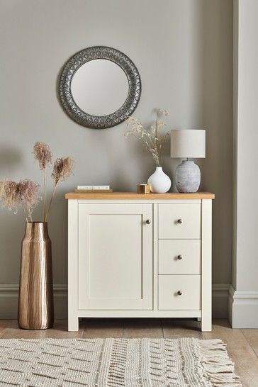 a white cabinet with two drawers and a mirror on the wall next to vases