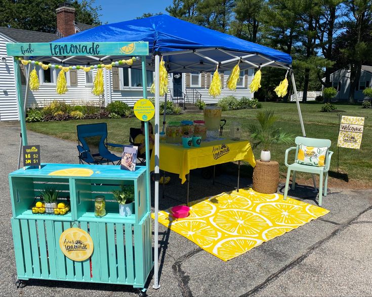 a lemonade stand is set up in front of a white house with blue awnings