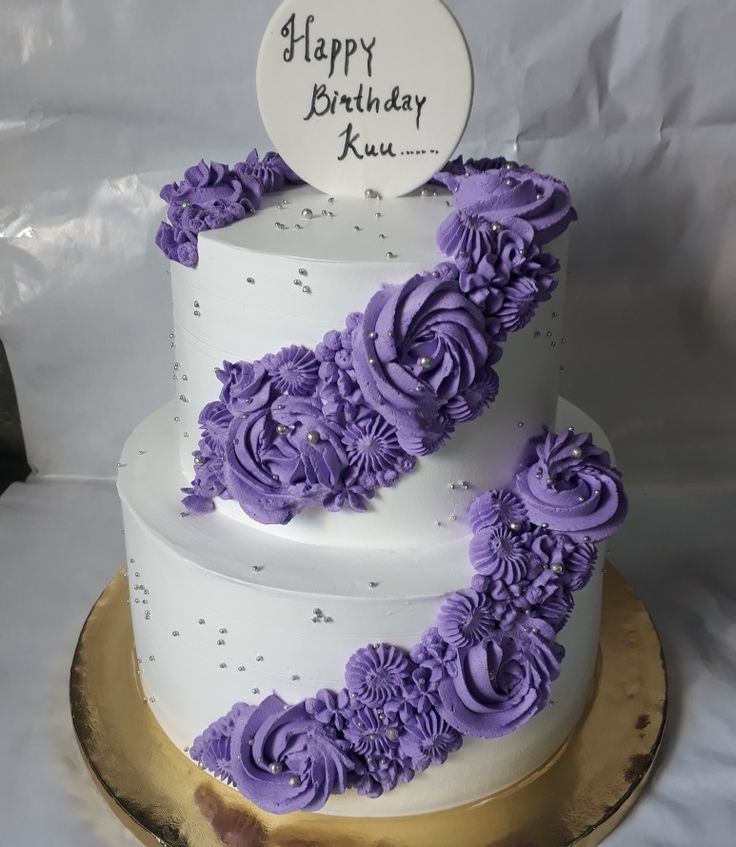 a three tiered white cake with purple flowers on the side and a happy birthday sign