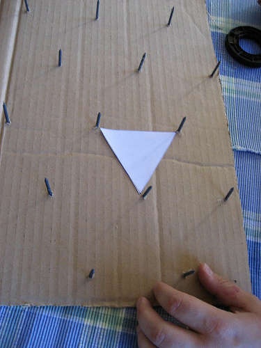 someone is making a paper triangle out of cardboard and some pins on the outside of it