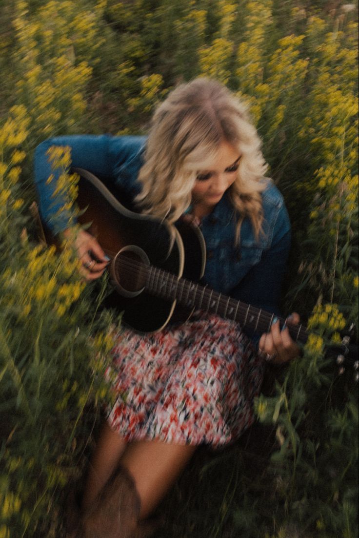 a woman sitting in the grass playing a guitar