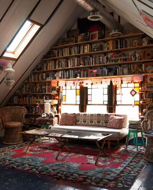 a living room filled with lots of furniture and bookshelves under a slanted ceiling