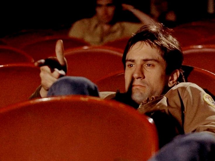 a man sitting in an auditorium with his hand up to the side and pointing at something