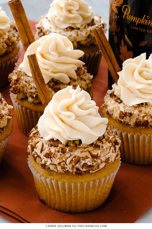 cupcakes with white frosting and cinnamon sticks on an orange napkin next to a bottle of booze