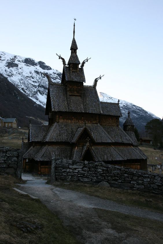 an old wooden church in the mountains with snow on the mountain behind it and a path leading up to it