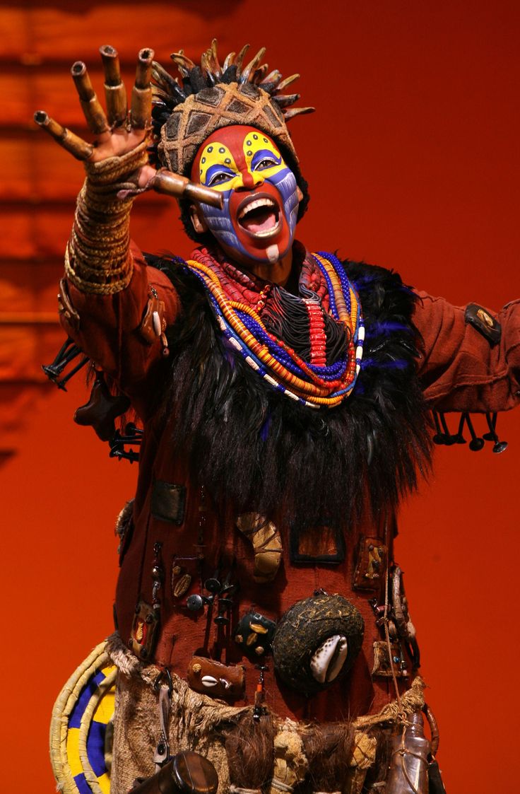 a man with painted face and body holding up his hands in the air while wearing an elaborate headdress