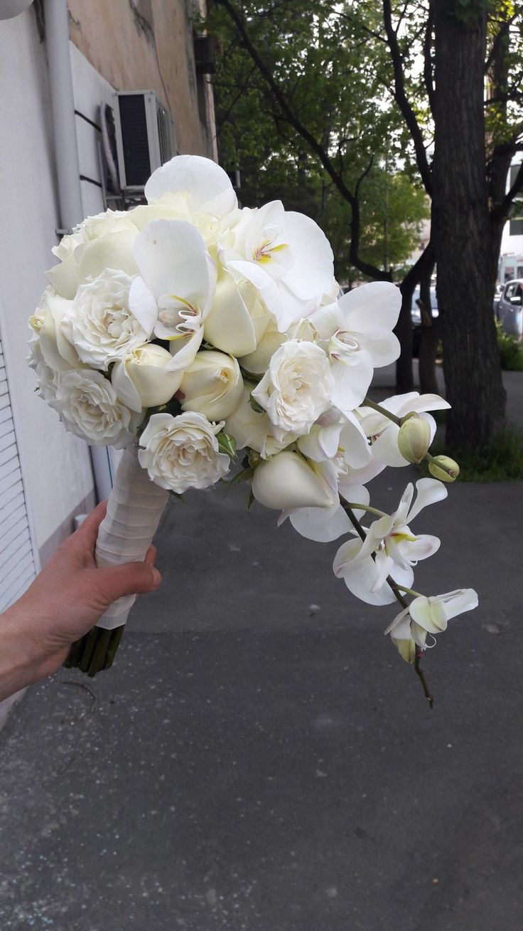 a bouquet of white flowers being held by someone's hand in front of a building