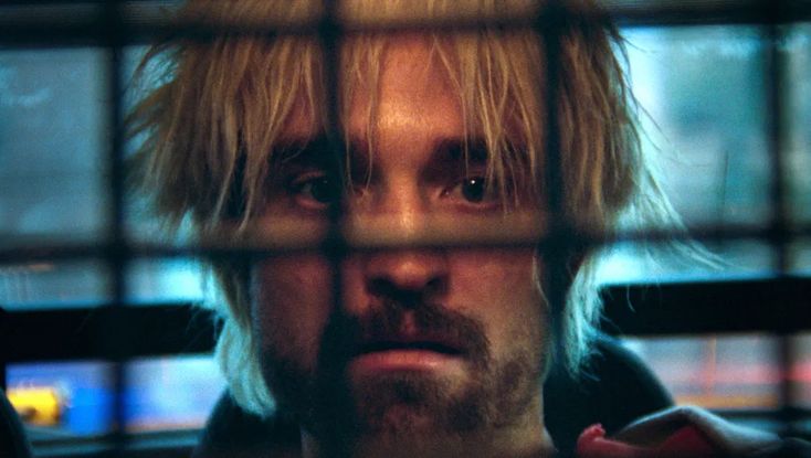 a man with blonde hair behind bars in a cage