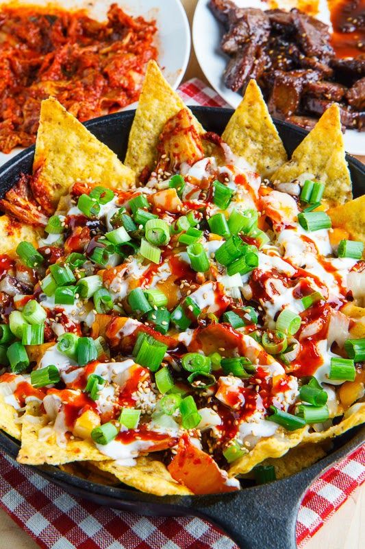 a skillet filled with nachos, cheese and green onions on a table