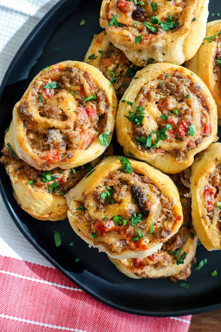 a black plate topped with mini pizzas on top of a red and white table cloth