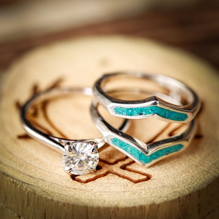 two silver rings with blue and white stones on them sitting on a piece of wood