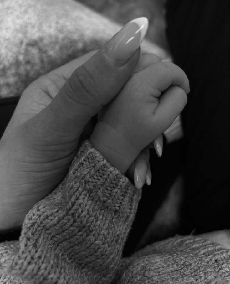 a black and white photo of a woman's hand holding the wrist of her baby