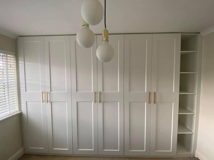 an empty room with white closets and hanging light fixtures on the wall above them